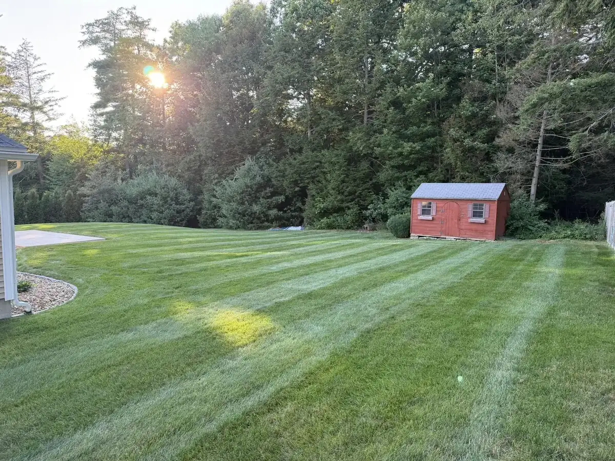 Striped backyard lawn around a shed and fenced yard in Southern New Hampshire