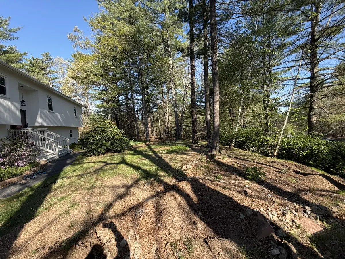 Eroded side yard with exposed rock and bare patches before regrading in Southern New Hampshire