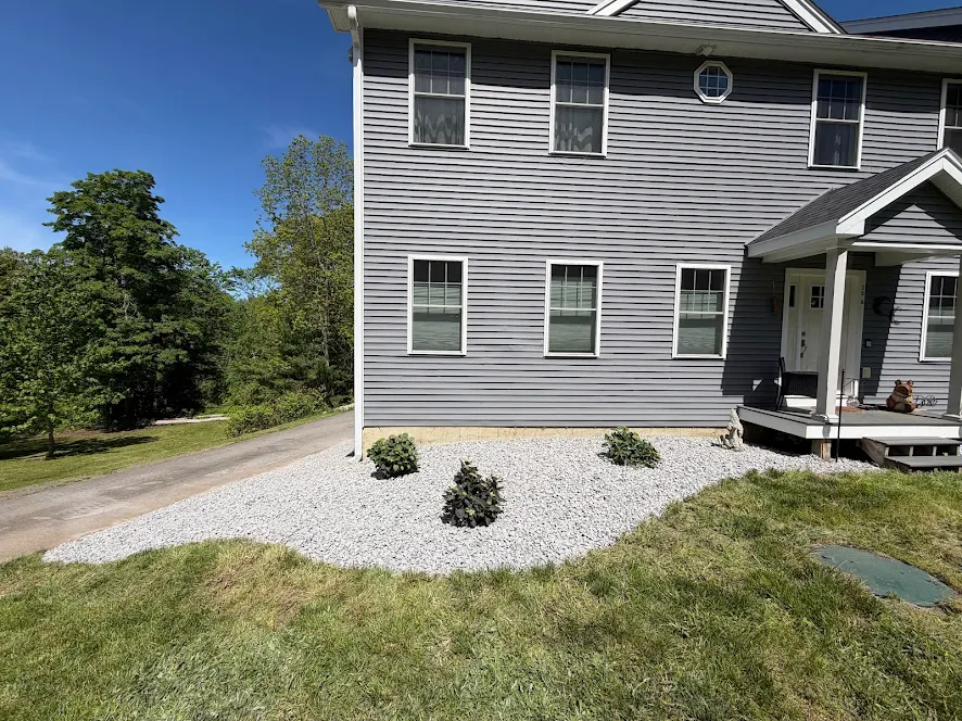 Finished white crushed stone foundation bed with new shrubs along the same gray colonial