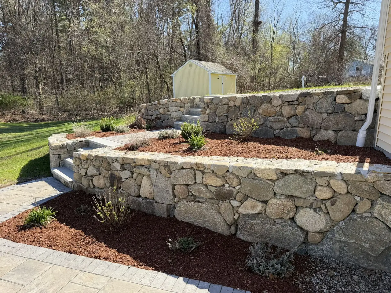 Fieldstone retaining wall with fresh red mulch and new plantings in Southern New Hampshire