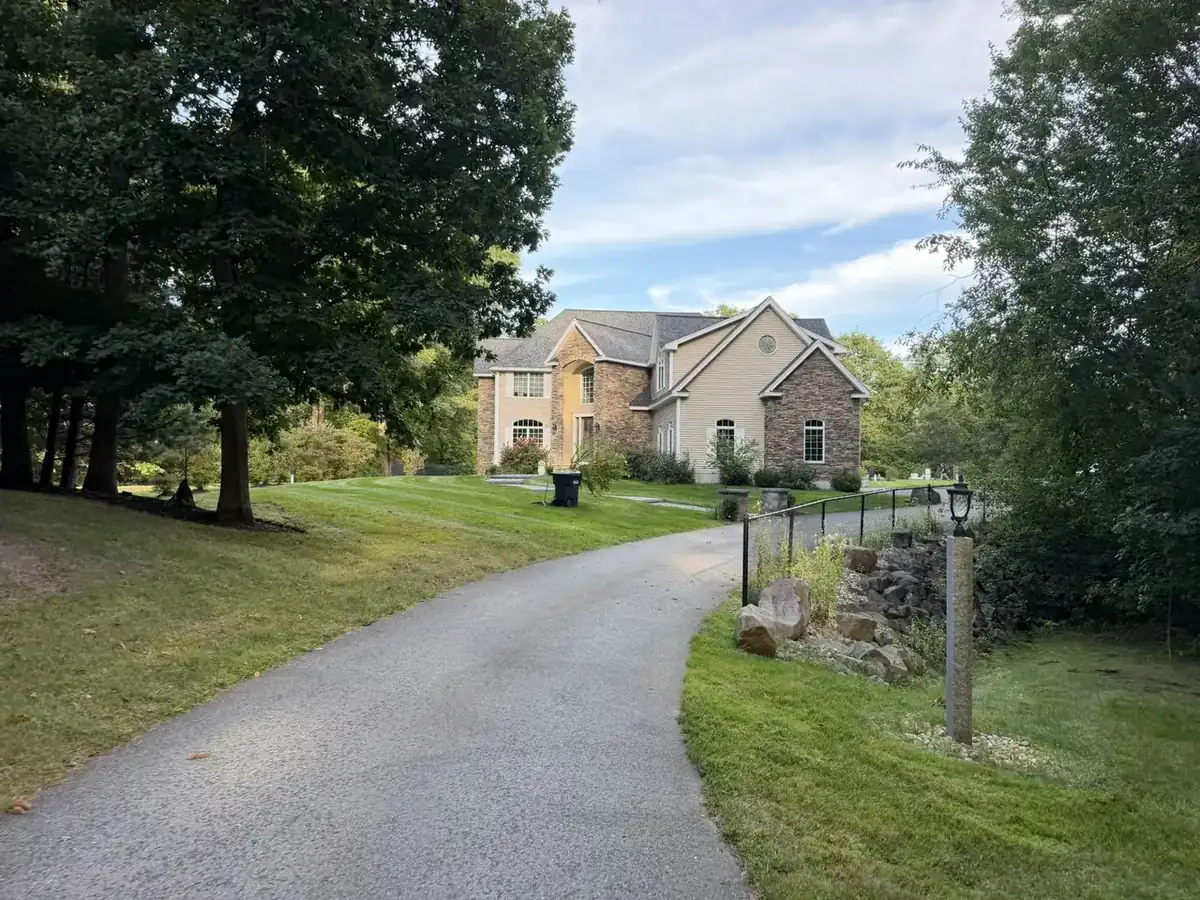 Stone-front colonial with a striped lawn and clean driveway edges in Southern New Hampshire