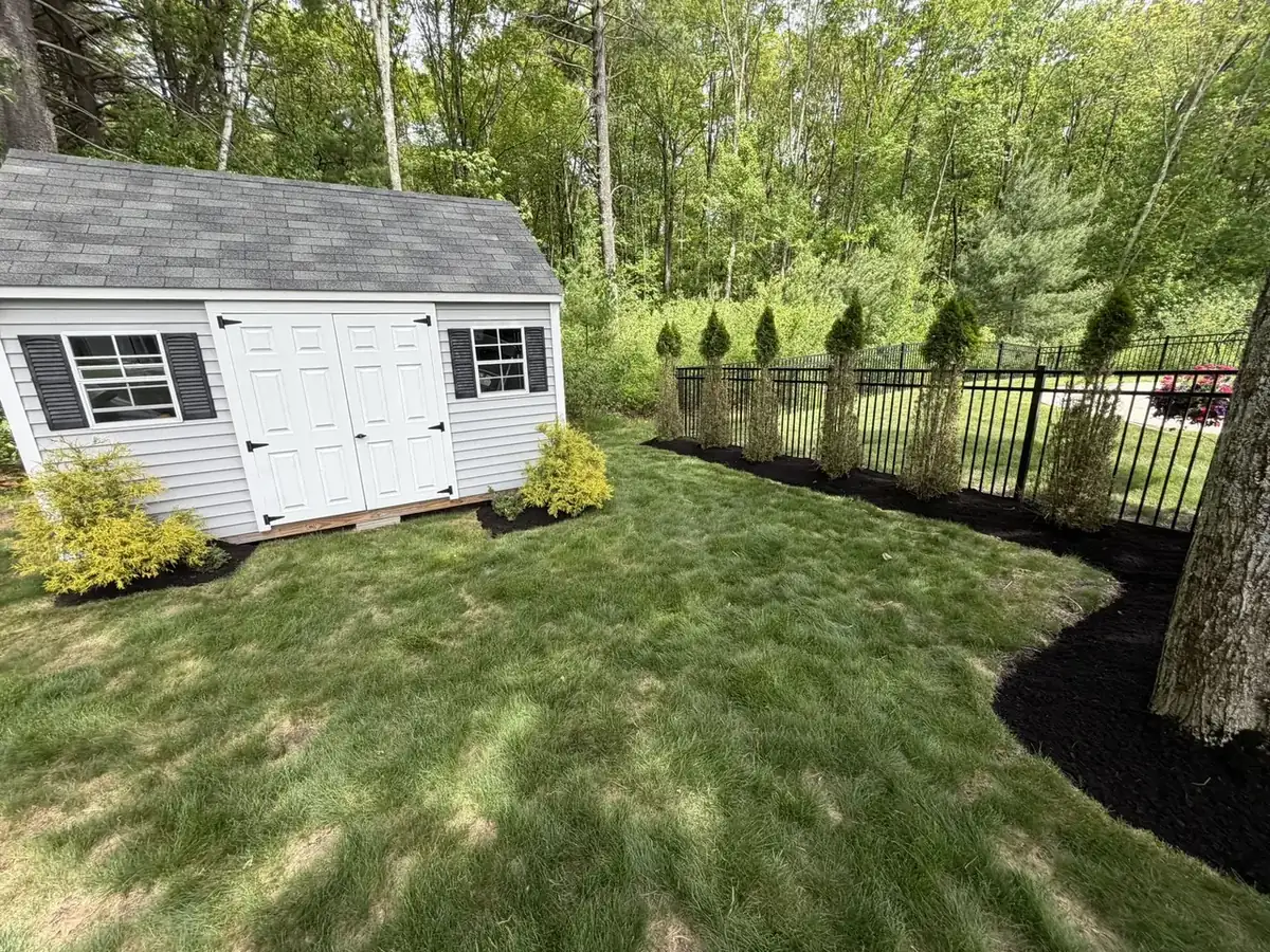 Black mulch bed along a shed with a striped lawn in Southern New Hampshire
