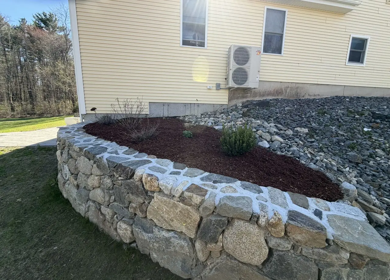 Curved fieldstone raised bed with mulch and a crushed stone drip edge in Southern New Hampshire